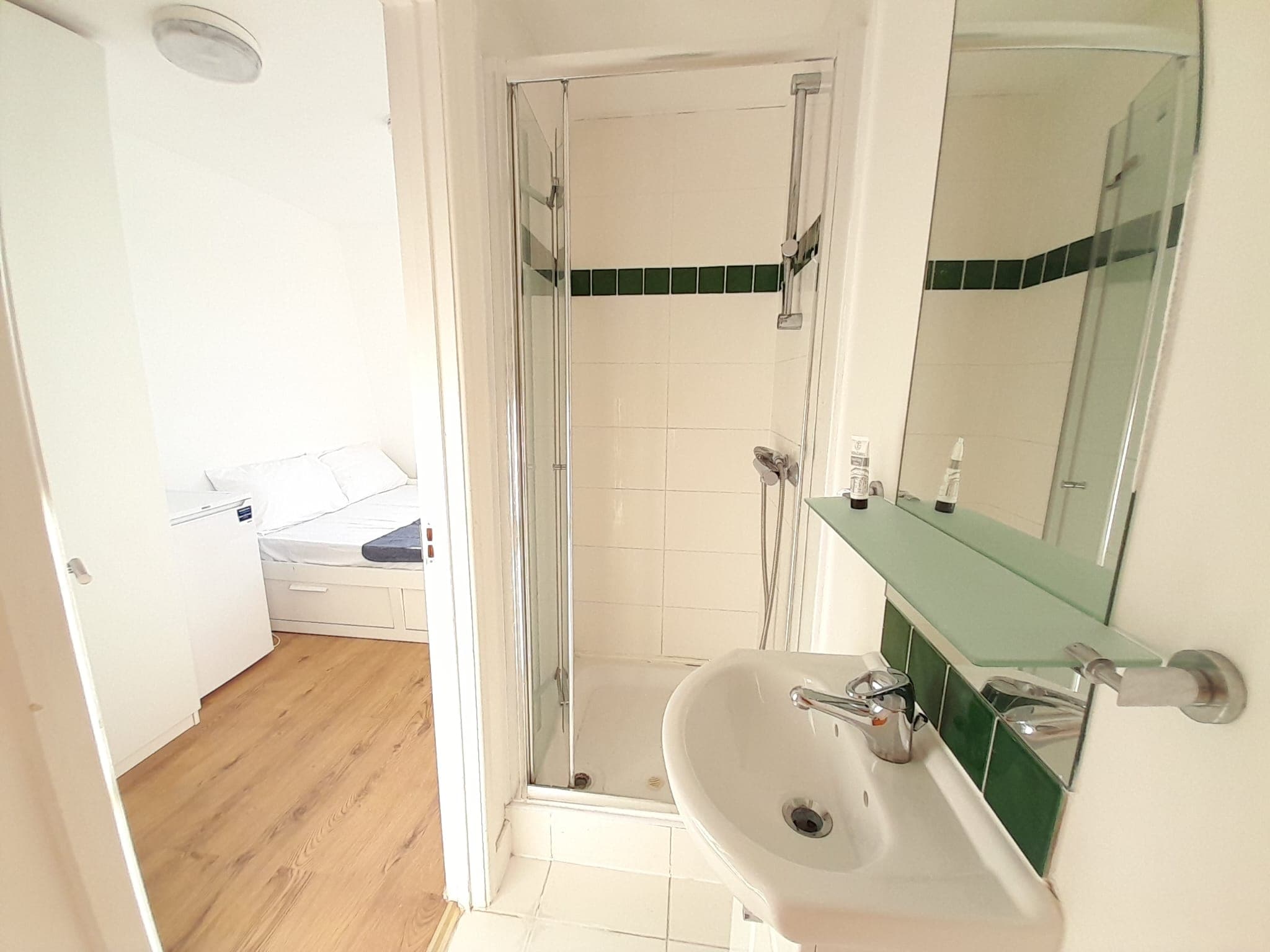 Small bathroom with a white sink and glass shower stall, opening into a bright bedroom.