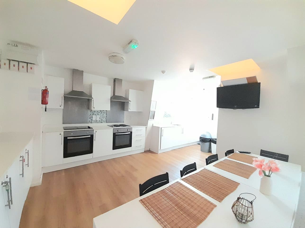Bright white kitchen with dual ovens, wood floors, and a dining table with pink flowers.