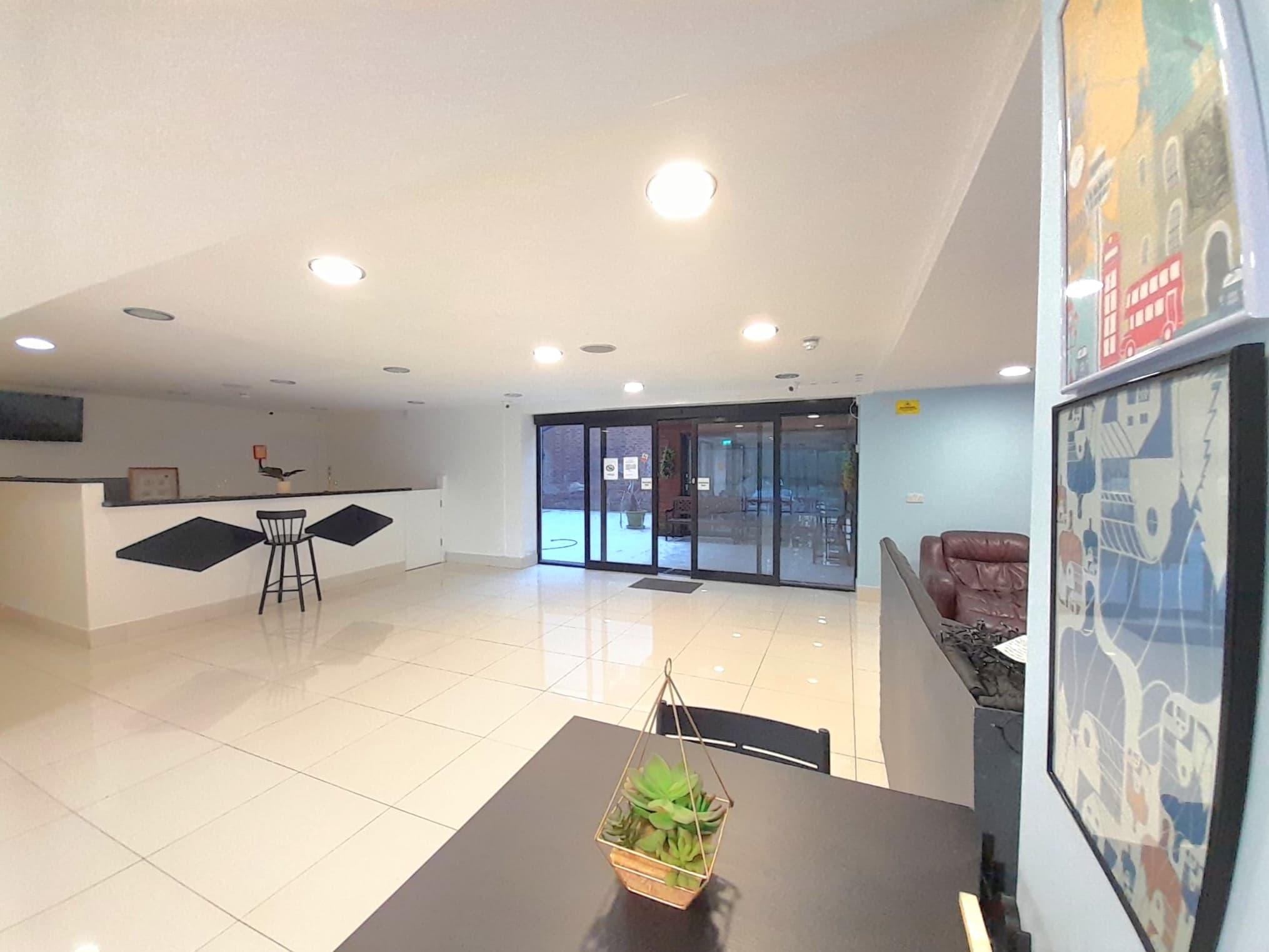 Bright modern lobby featuring white tiled floors, a reception desk, and large glass sliding doors.